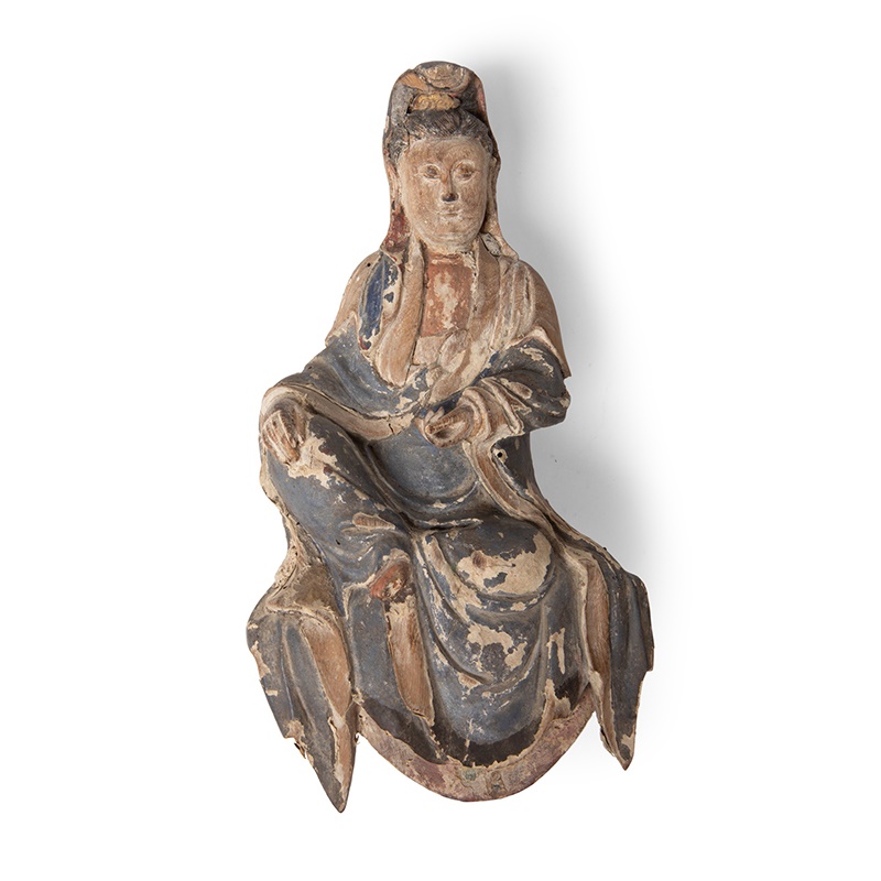 LOT 10 | WOODEN SCULPTURE OF WATER-AND-MOON GUANYIN | QING DYNASTY, 17TH CENTURY | 清 木雕水月觀音坐像 carved seated in lalitasana or royal ease pose, the right arm resting on the knee, the left hand half raised in front of the chest, wearing layers of robes naturally draped downwards, finely incised hair arranged in a high chignon and covered by a cowl, her benign face finely carved with downcast eyes, finely closed lips and elongated ears, with remnant of red and black pigments (Qty: 1) 24.5cm high | £600 - £800 + fees